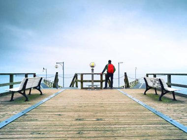 Turist ahşap deniz pier üzerine kırmızı sırt çantası ile. Trekking takım elbiseli adam