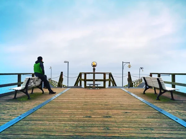 Mann auf hölzernem Maulwurf im Hafen an einem nebligen Herbsttag. Tourist am Geländer. — Stockfoto