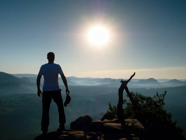 Wanderer im grauen T-Shirt mit roter Mütze in der Hand auf felsigem Gipfel. — Stockfoto