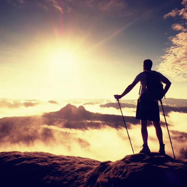 Höga backpacker med stolpar i hand. Soliga dimmiga gryning i klippiga bergen. Hiker med ryggsäck stå på steniga utsiktsplats över dalen. Levande och starka vinjettering effekten. — Stockfoto