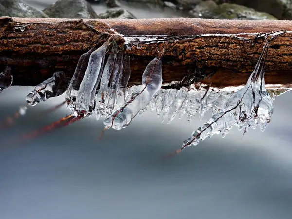 Largos carámbanos cuelgan sobre el agua helada oscura del arroyo de montaña . — Foto de Stock