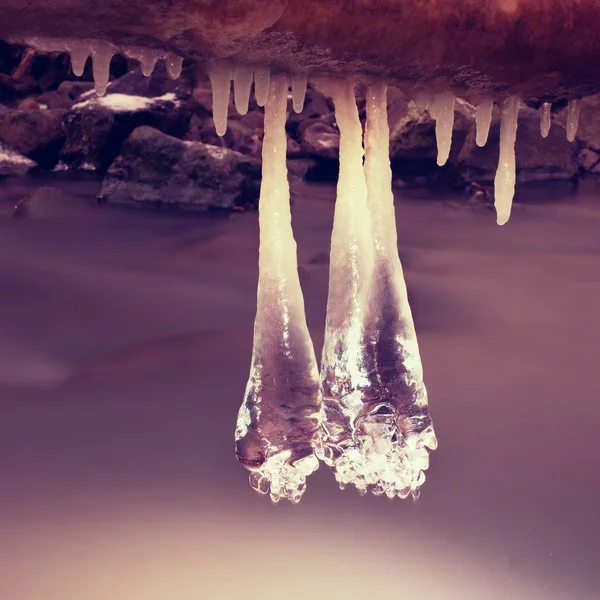 I ghiaccioli lunghi pendono su tronco caduto sopra acqua scura — Foto Stock