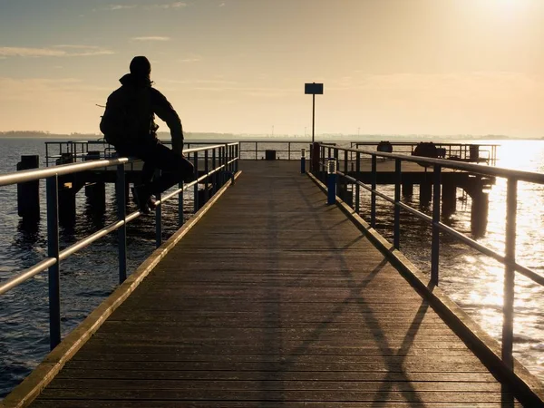 Touristen sitzen auf dem Handlauf des Maulwurfs und fotografieren die Holzpromenade — Stockfoto