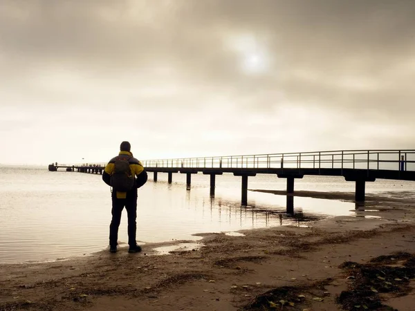 Hiker with backpack alone on sandy beach, sunrise above sea bridge. — Stock Photo, Image