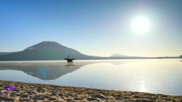 Hombre alto con gafas de sol, gorra de béisbol roja y ropa deportiva negra azul está corriendo y haciendo ejercicio en la playa al mediodía. Deporte hombre activo estirar las piernas y el cuerpo en la playa del lago de montaña . — Vídeos de Stock