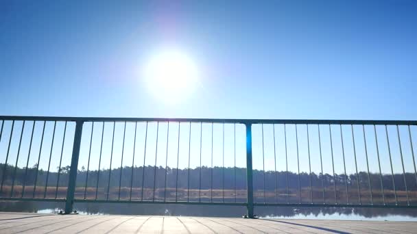 Lång man med solglasögon, röd mössa och bue svart sportkläder körs på stål ledstång på bron. Silhuetten av sport aktiva mannen kör och tränar på solig blå himmel bakgrund. — Stockvideo