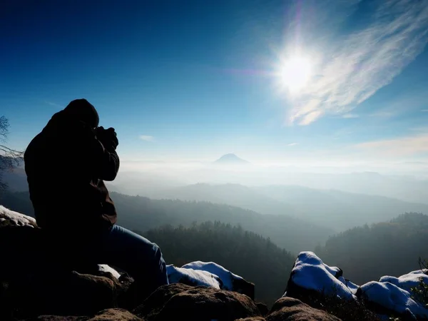 Tall  man is taking photo by mirror camera on neck. Snowy rock — Stock Photo, Image