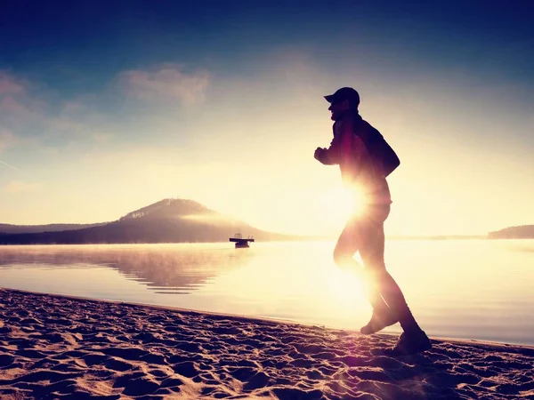 Silueta del hombre activo deportivo corriendo en la playa del lago al amanecer. Estilo de vida saludable . — Foto de Stock