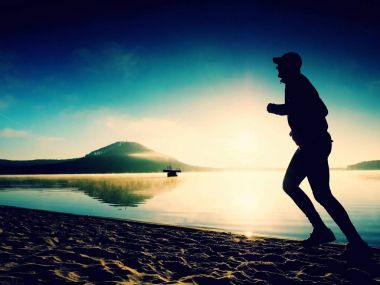Göl kumsalda güneş doğarken koşan spor etkin adam silüeti. Sağlıklı yaşam tarzı. 