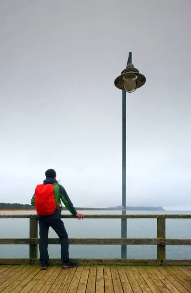 Turista s červeným batohem na dřevěné moře mola. Muž v obleku trekingové — Stock fotografie