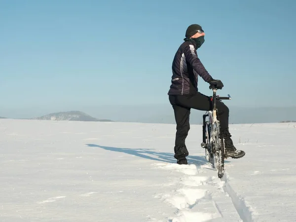 Motociclista empurrando mountain bike na neve deriva. Congele o tempo de inverno ensolarado. Motociclista está empurrando bicicleta na neve profunda — Fotografia de Stock