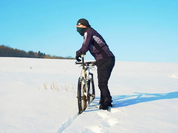 Motociclista empurrando mountain bike na neve deriva. Congele o tempo de inverno ensolarado. Motociclista está empurrando bicicleta na neve profunda — Fotografia de Stock