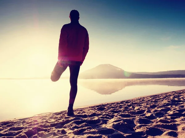 Ο άνθρωπος που ασκεί στην παραλία. Σιλουέτα του δραστήριος άνδρας άσκηση και διατάσεις στη λίμνη — Φωτογραφία Αρχείου