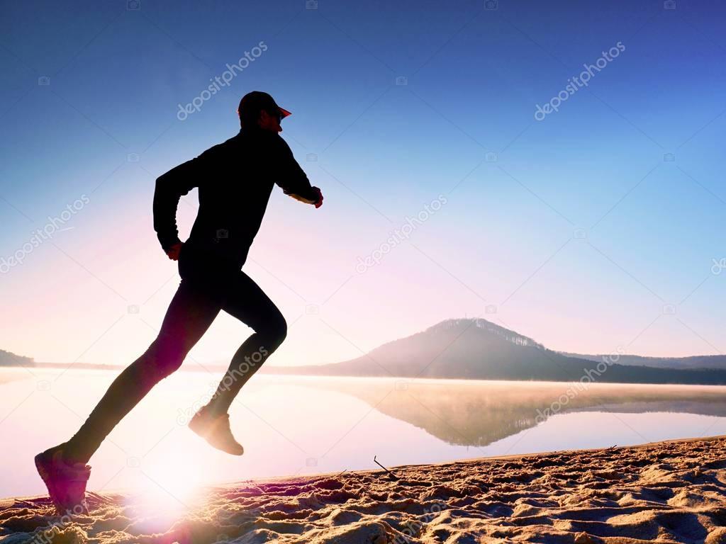 Man exercising on beach.  Silhouette of active man exercising  and stretching at lake