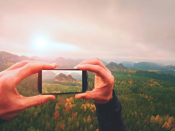 Smart phone mobile photography of misty landscape. Focus to detail with phone in man hands.