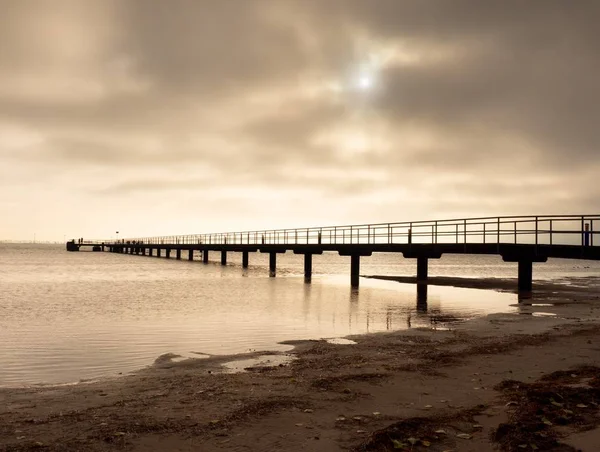 Långa träbrygga vid kusten, kall morgon, lugn tyst dag — Stockfoto