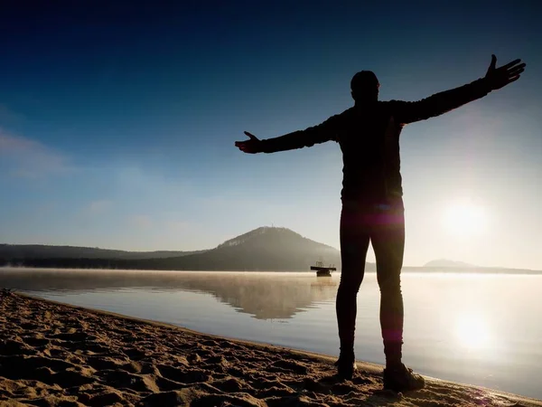 Man uit te oefenen op strand. Silhouet van actieve man uit te oefenen en rekken in lake — Stockfoto