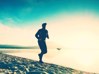 Göl kumsalda güneş doğarken koşan spor etkin adam silüeti. Sağlıklı yaşam tarzı. 