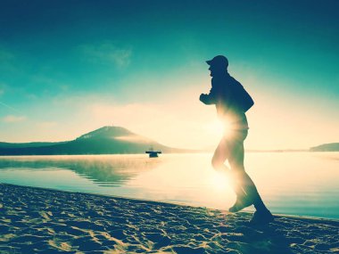 Göl kumsalda güneş doğarken koşan spor etkin adam silüeti. Sağlıklı yaşam tarzı. 