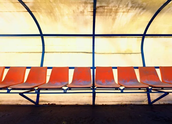 Sedili in plastica vintage sulla panchina dei giocatori dello stadio all'aperto, sedie con vernice usurata sotto il tetto giallo . — Foto Stock