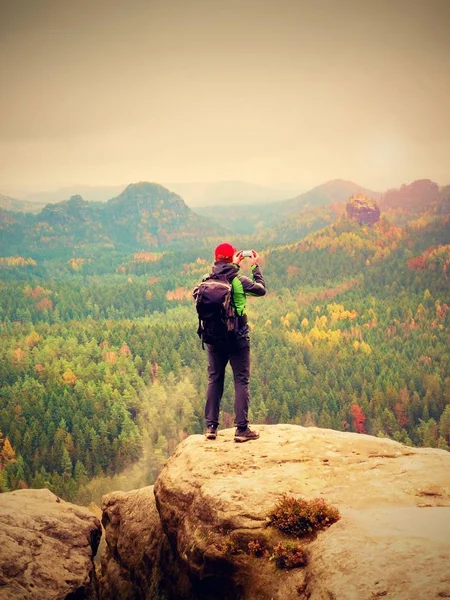 Turista com mochila ficar cliff e leva fotos com telefone inteligente do vale das chuvas. — Fotografia de Stock