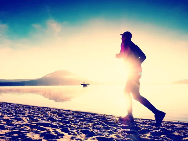 Sylwetka sport active człowiek działa na plaży nad jeziorem o wschodzie słońca. Zdrowy styl życia. — Zdjęcie stockowe