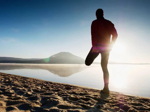 Hombre haciendo ejercicio en la playa. Silueta del hombre activo haciendo ejercicio y estirándose en el lago — Foto de Stock