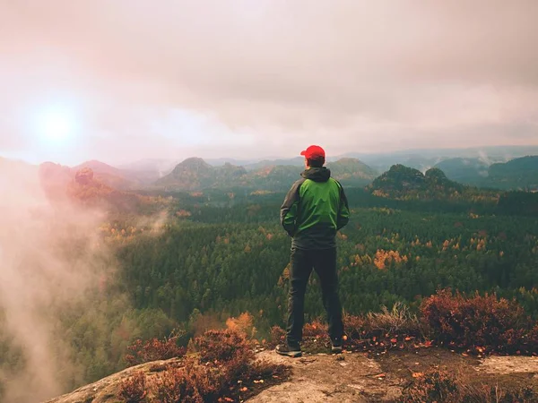 Uomo turista soggiorno sulla vetta della roccia tagliente. Alone escursionista in berretto rosso e giacca verde godere della vista — Foto Stock