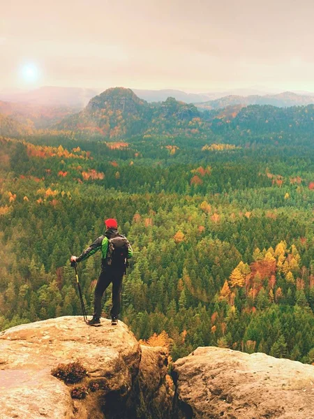 Ein großer Wanderer mit roter Mütze, Stöcken in der Hand und großem Rucksack steht auf einem Felsen. Nebel im Frühling — Stockfoto