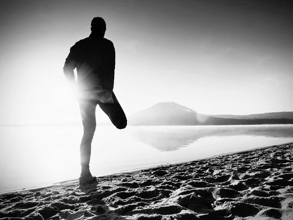 Człowieka, ćwiczenia na plaży. Sylwetka człowieka aktywnych ćwiczeń i rozciągający się nad jeziorem — Zdjęcie stockowe