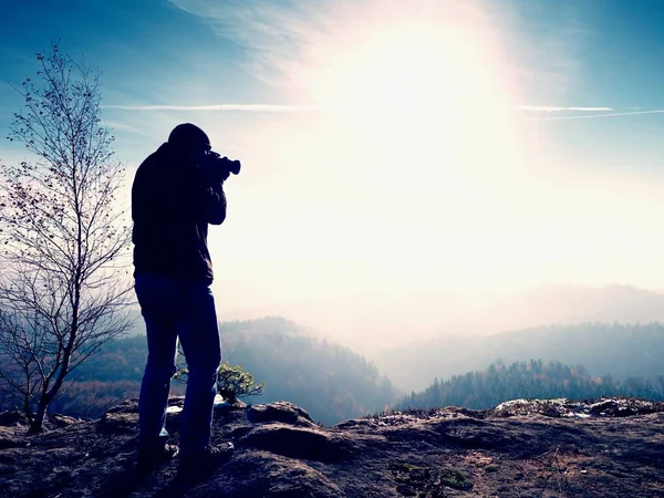 Tall  man is taking photo by mirror camera on neck. Snowy rocky peak of mountain. — Stock Photo, Image