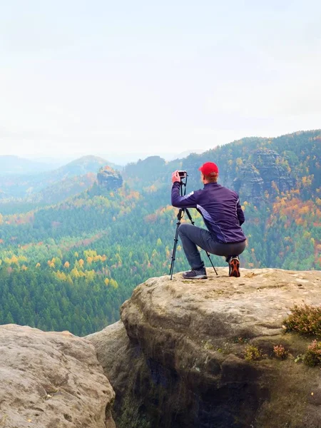 Фотограф на открытом воздухе с треногой и камерой на каменном мышлении. Осенняя долина — стоковое фото