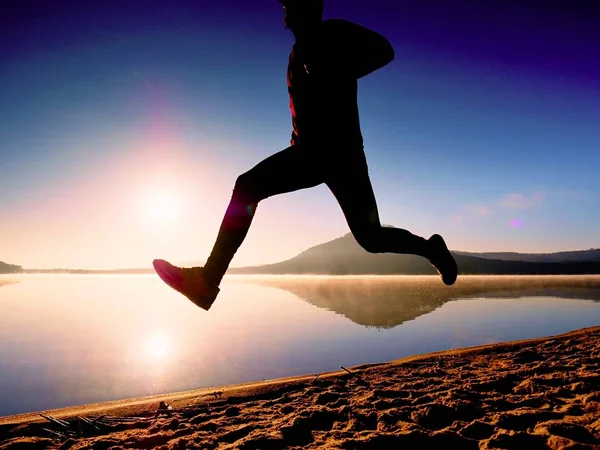 Man exercising on beach.  Silhouette of active man exercising  and stretching at lake