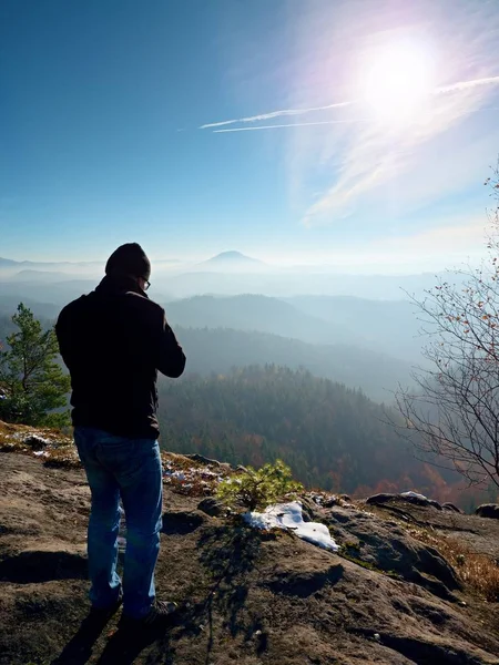 Tall  man is taking photo by mirror camera on neck. Snowy rocky peak of mountain. — Stock Photo, Image