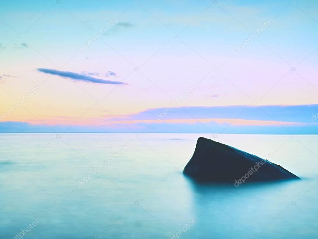 Alone stone in smooth sea. Beautiful seascape with low lightt. Sea and rock at the sunset.