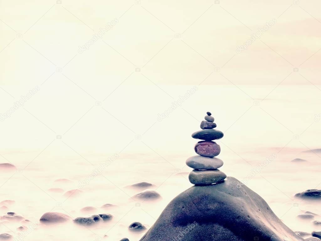 Stacked rounded stones at sea. Polished pebbles on dark wet rock,  smooth water