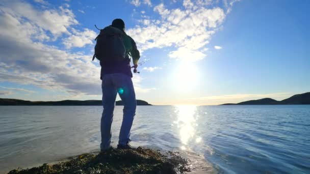 Le pêcheur avec sac à dos sportif vert vérifie l'équipement de pêche. L'homme prépare pousser appât sur la ligne de pêche et jeter leurre loin dans l'eau de mer calme. Pêcheur profiter des activités sportives après-midi . — Video