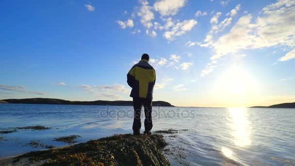 Amigos hablan de pesca y senderismo. Joven pescador en el mar hablar con el hombre excursionista con bastones de trekking y mochila deportiva verde. Hombres disfrutando de la pesca con hermosa puesta de sol — Vídeo de stock