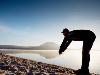 Kumsalda egzersiz adam. Egzersiz ve gölde germe etkin adam silüeti