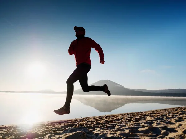 Homem a correr à beira-mar no crepúsculo. atleta corredor correndo à beira-mar. Sílhueta de aptidão desportiva — Fotografia de Stock