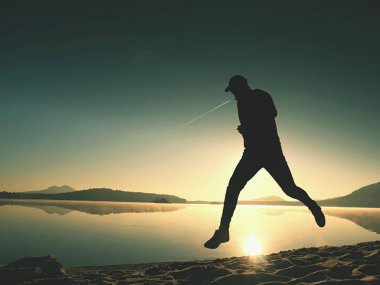 Plajda çalışan adam. Kumlu bir plaj üzerinde gündoğumu sırasında adam koşu beyzbol şapkası çalıştırmak sporcu. Gün batımında sahilde atlama adam