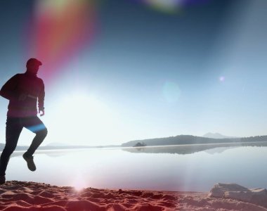 Plajda çalışan adam. Kumlu bir plaj üzerinde gündoğumu sırasında adam koşu beyzbol şapkası çalıştırmak sporcu. Gün batımında sahilde atlama adam