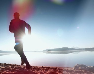 Plajda çalışan adam. Kumlu bir plaj üzerinde gündoğumu sırasında adam koşu beyzbol şapkası çalıştırmak sporcu. Gün batımında sahilde atlama adam