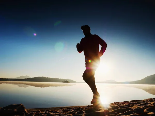 Hombre corriendo en la playa. Deportista corriendo en gorra de béisbol, trotando chico durante el amanecer sobre la playa de arena. Hombre saltando en la playa al atardecer — Foto de Stock