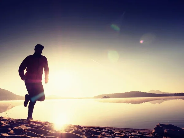Hombre corriendo en la playa. Deportista corriendo en gorra de béisbol, trotando chico durante el amanecer sobre la playa de arena. Hombre saltando en la playa al atardecer — Foto de Stock