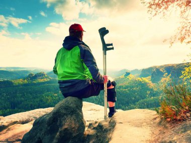 Yorgun bir adam turist sit immobilizer veya rock, zarar diz ile tıp direği tut. Açık orman manzara