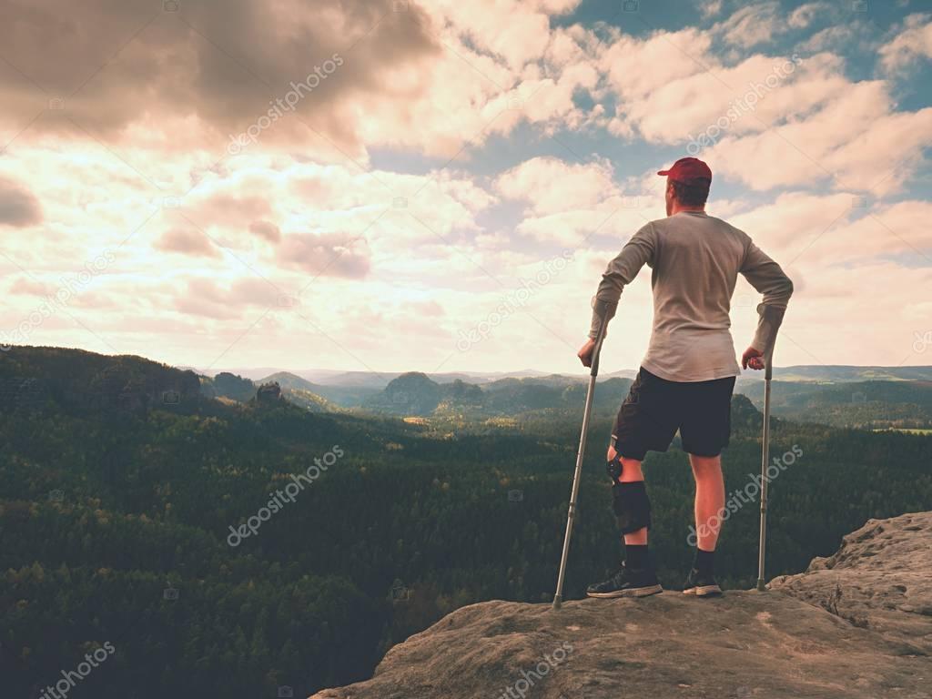 Happy man with broken leg in immobilizer and medicine pole stay finnaly on  peak.