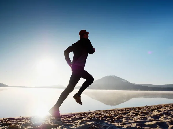 Hombre alto corriendo a lo largo de la orilla del mar en la mañana. Jogging masculino saludable en la playa . — Foto de Stock