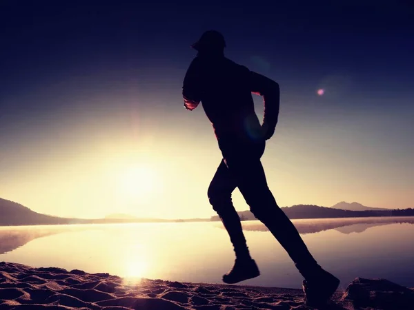 Silhouet van actieve man uit te oefenen en rekken op het lake strand bij zonsopgang. — Stockfoto