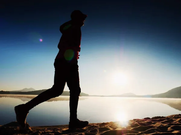 Silhouette de l'homme actif faisant de l'exercice et s'étirant sur la plage du lac au lever du soleil . — Photo